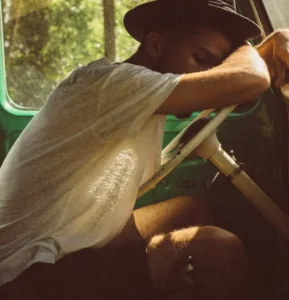 Junger Mann mit Hut schläft in seinem Auto.