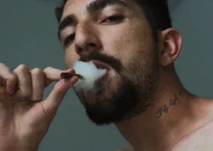 Ein junger Mann blickt in die Kamera und kifft.