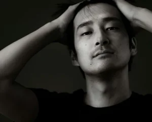 Ein asiatischer Mann wird in schwarz/weiß gezeigt und blickt niedergeschlagen in die Kamera.