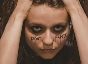 Eine verstörte junge Frau blickt in die Kamera und hat "Don't Panic" im Gesicht stehen.